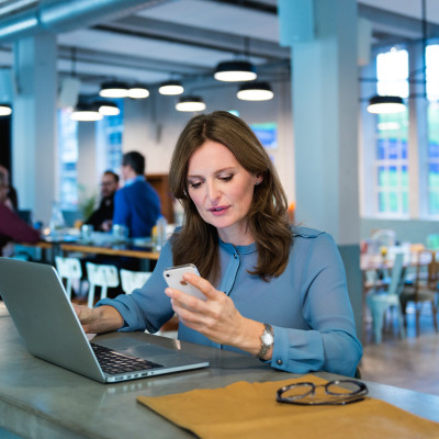 Vrouw achter laptop met telefoon in haar hand